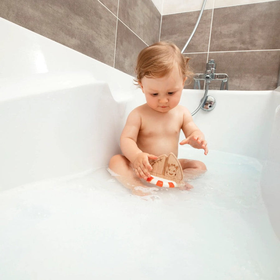 Picture of a baby in a bathtub playing with the Sophie La Girafe rubberwood boat toy
