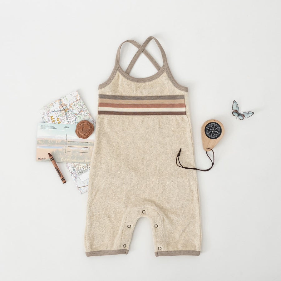 Picture of the overalls on a white surface with other objects arrayed around them, including a map of New Mexico, a postcard, a compass, a brown crayon, and a decorative blue butterfly.