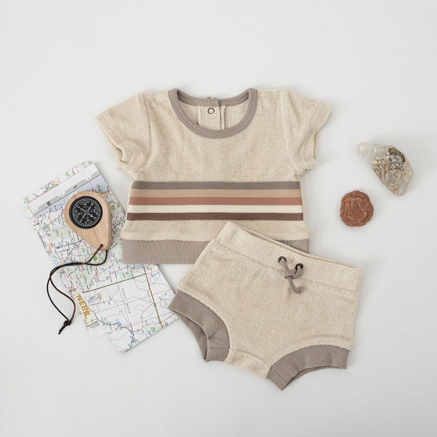 Picture of the shorts and tee set laying on a white surface with an array of items around them, including pretty rocks, a compass, and a map.