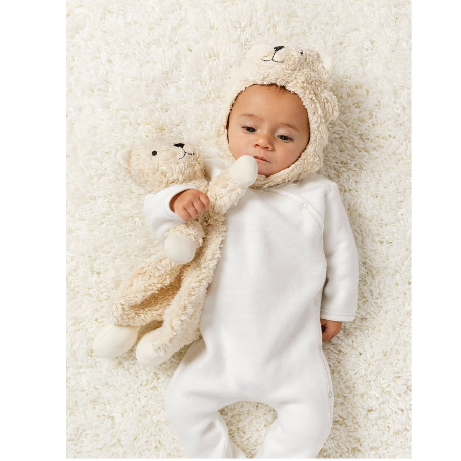 picture of a baby wearing a white kimono coverall and a bear hat holding the bear lovey
