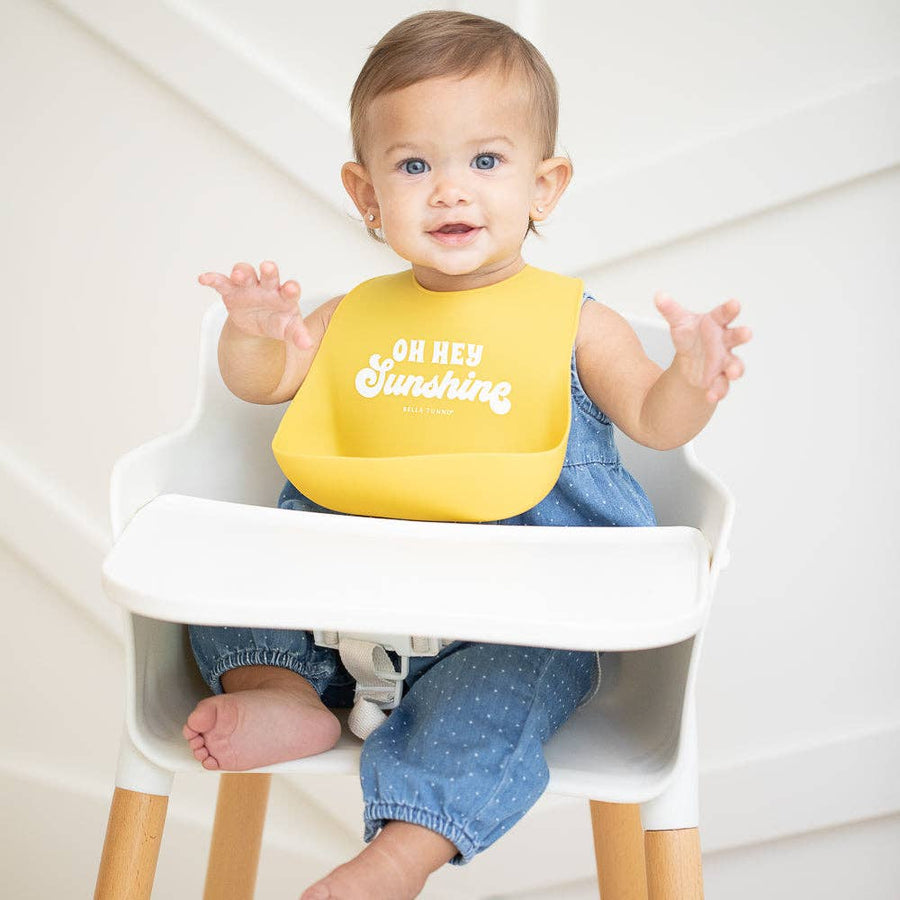 Baby in a high chair wearing a yellow bib with 'Oh Hey Sunshine' text.