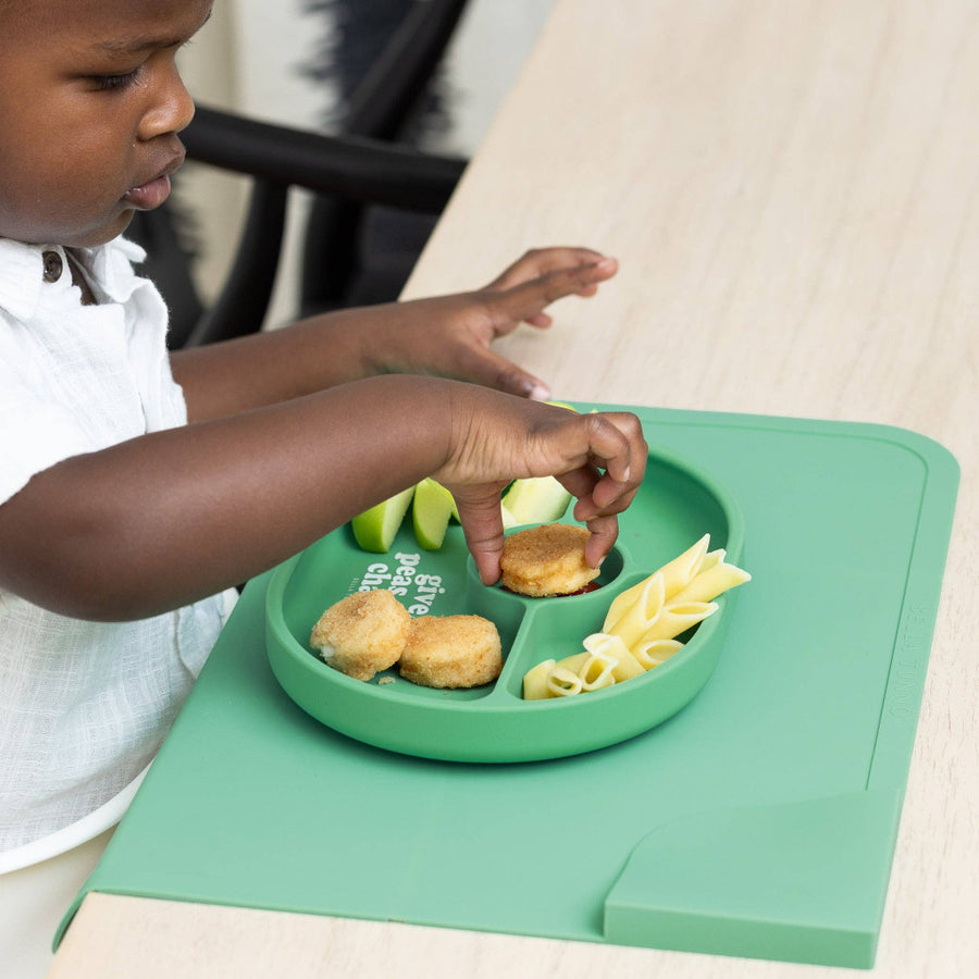 Child using a green divided plate with food on a matching placemat.