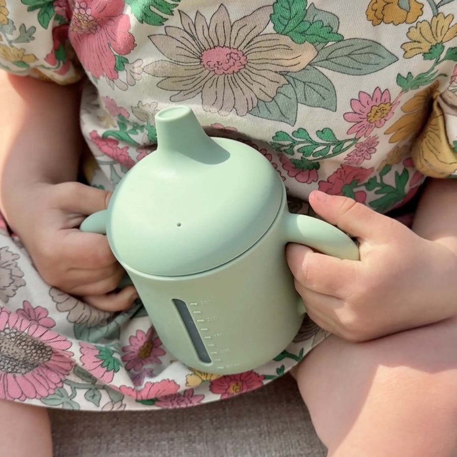 Child holding a light green cup with a floral-patterned outfit