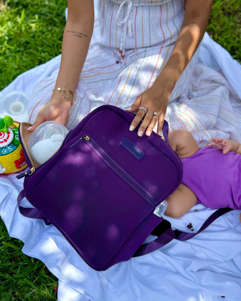 Person holding a purple bag on a grassy field with a baby in a purple outfit.