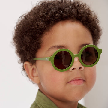 Child wearing green sunglasses with a plain background