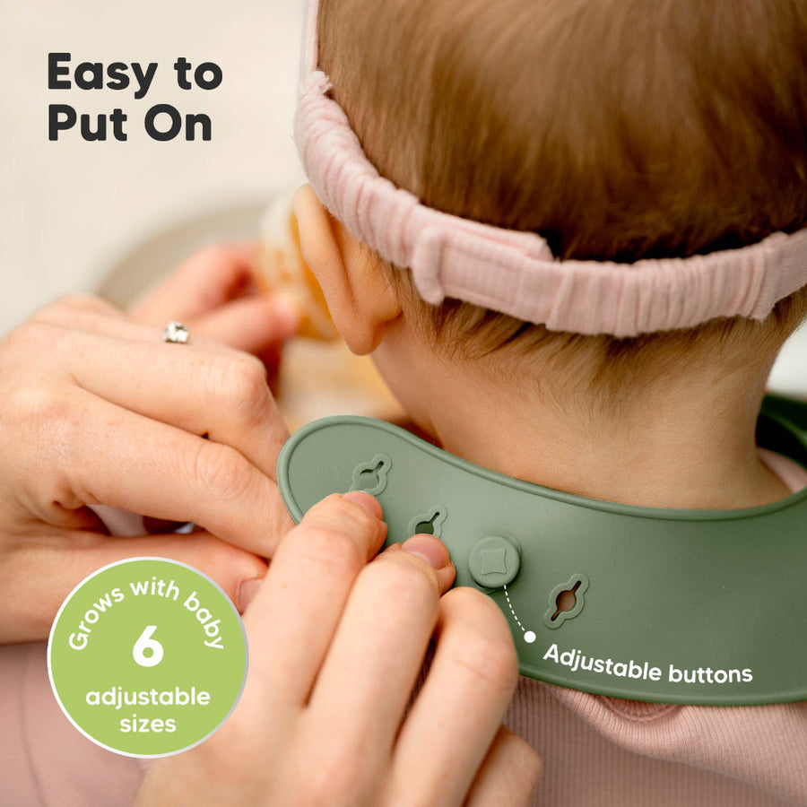Baby wearing a pink headband with a green bib with adjustable buttons, being adjusted by an adult hand.