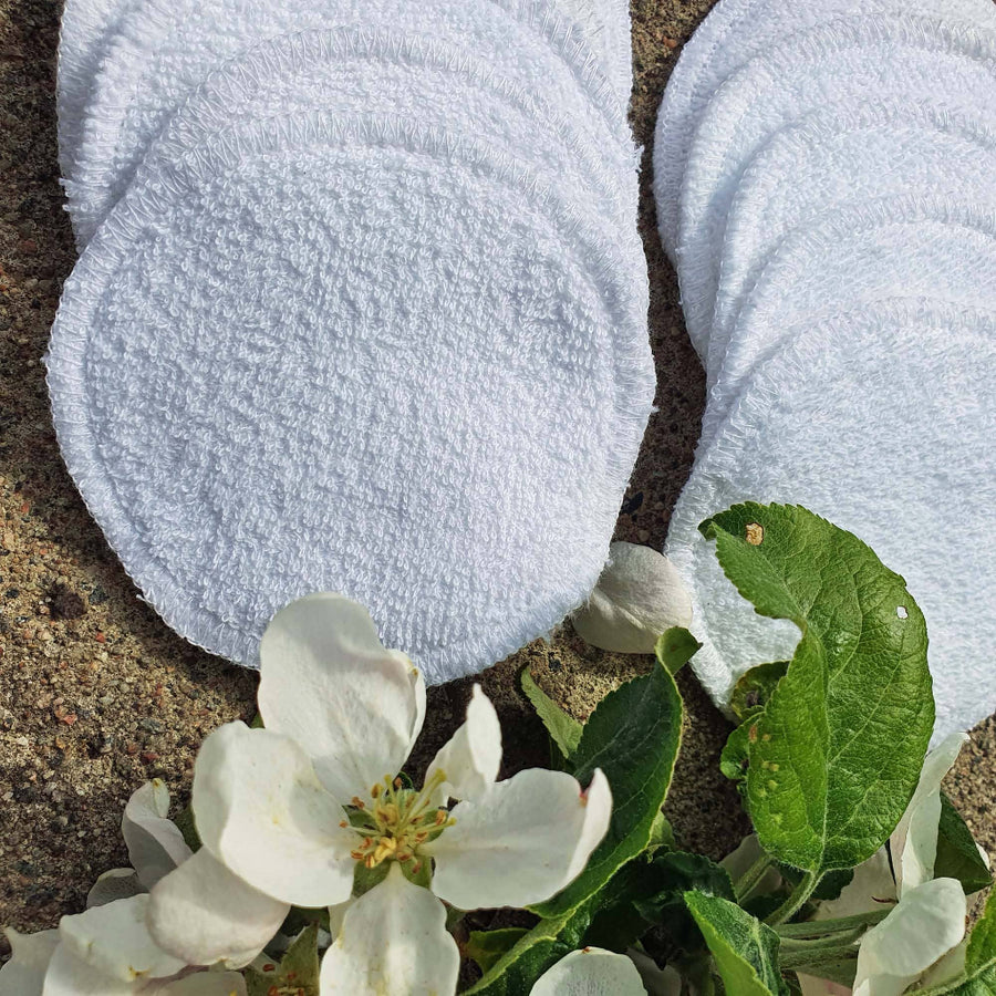 White round cloths on a textured surface with green leaves and white flowers.