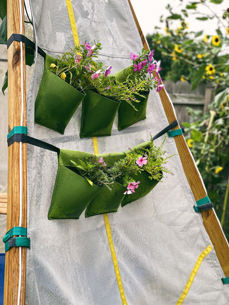 Green hanging planters with flowers attached to a wooden frame against a garden backdrop.