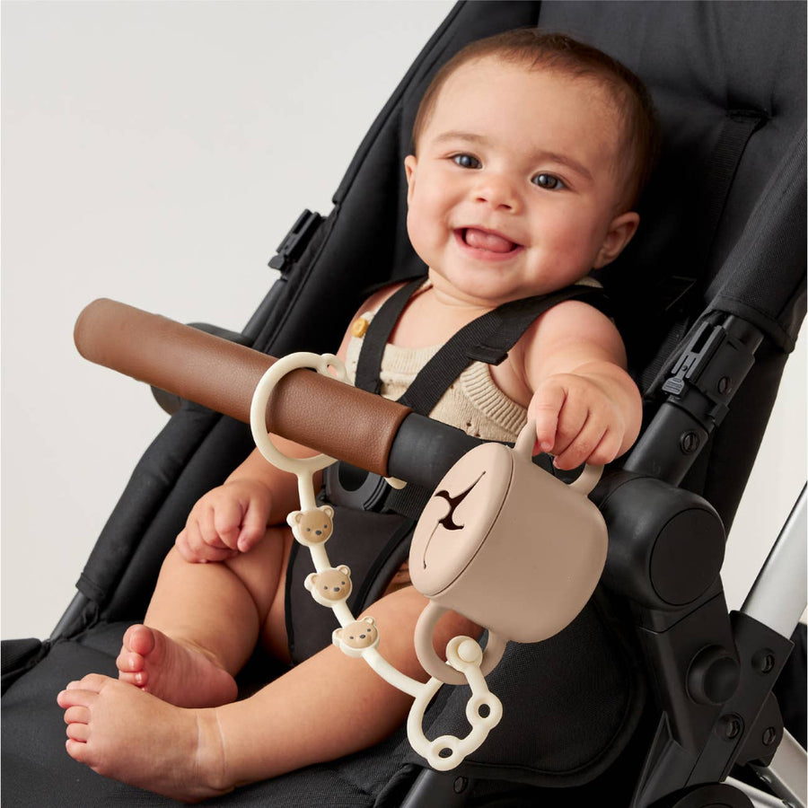 Baby sitting in a stroller with a toy attached to the handle
