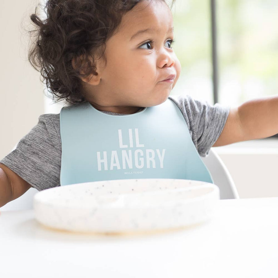 Child wearing a bib with 'LIL HANGRY' text, sitting at a table.