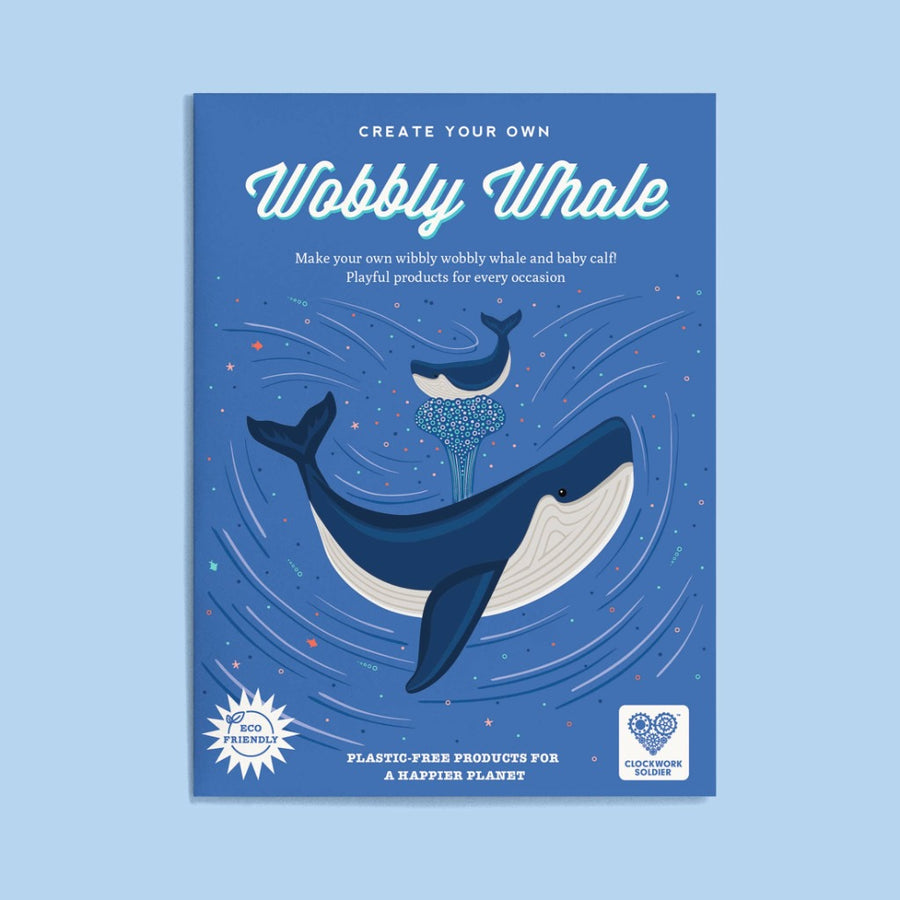 Image shows the packaging envelope for the Create Your Own Wobbly Whale, against a blue background. It is blue with an illustration of a spouting blue whale amidst tiny multi-colored stars, with a smaller whale borne aloft on the spout
