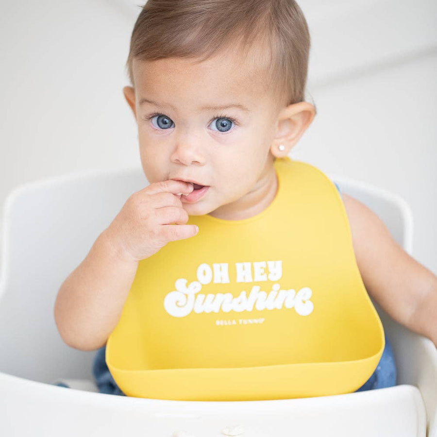 Baby wearing a yellow bib with 'Oh Hey Sunshine' text, sitting in a high chair.