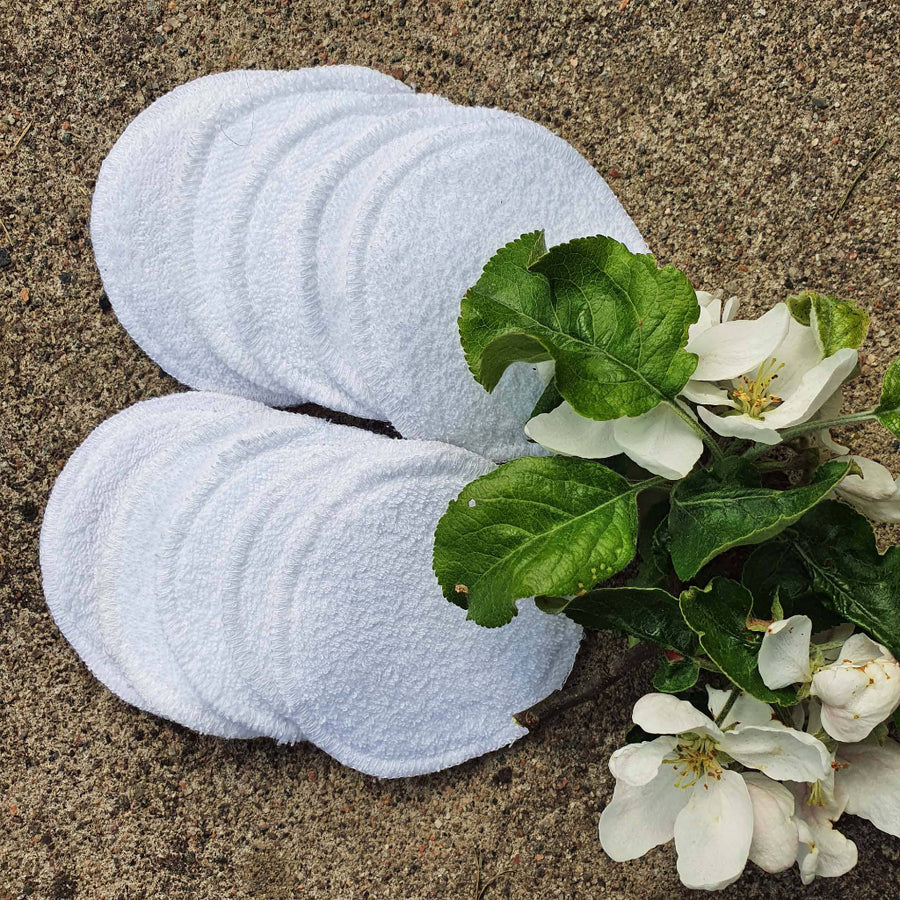 White towels on sand with green leaves and white flowers
