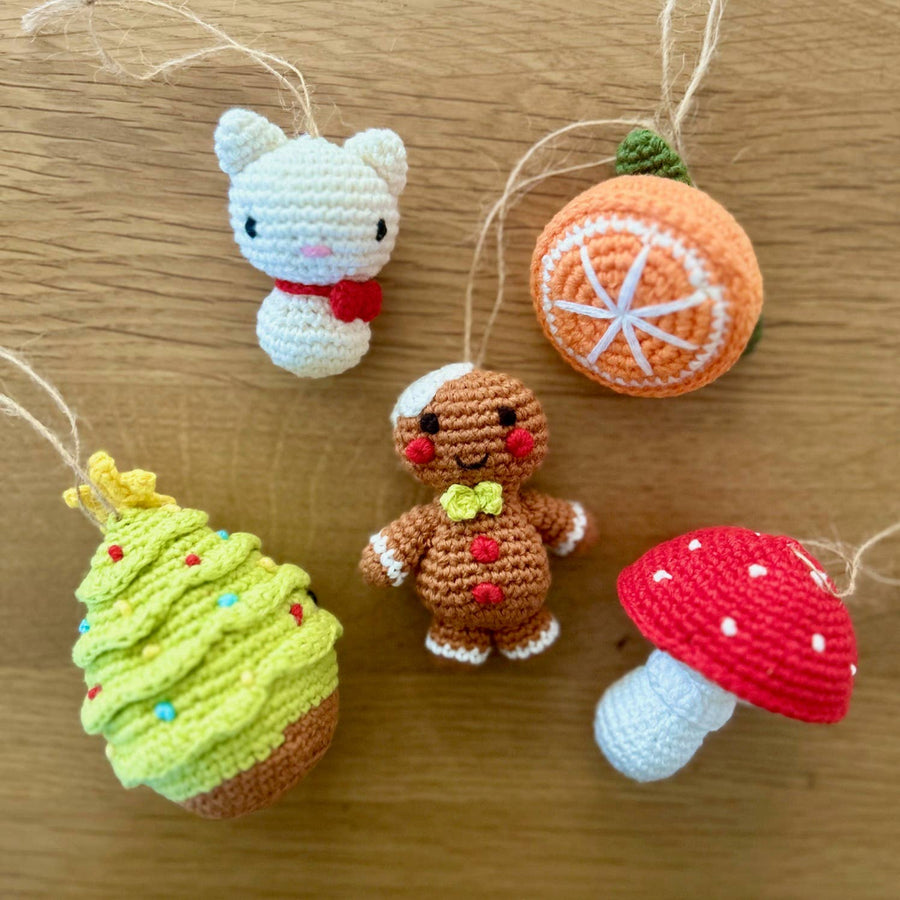 Set of crochet ornaments including a cat, gingerbread man, orange, cupcake, and mushroom on a wooden surface.