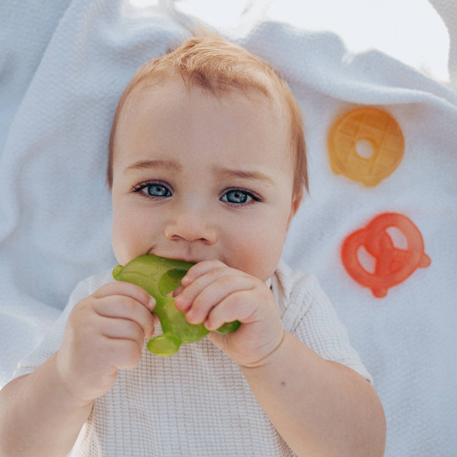 Baby chewing on a green object with colorful teethers in the background
