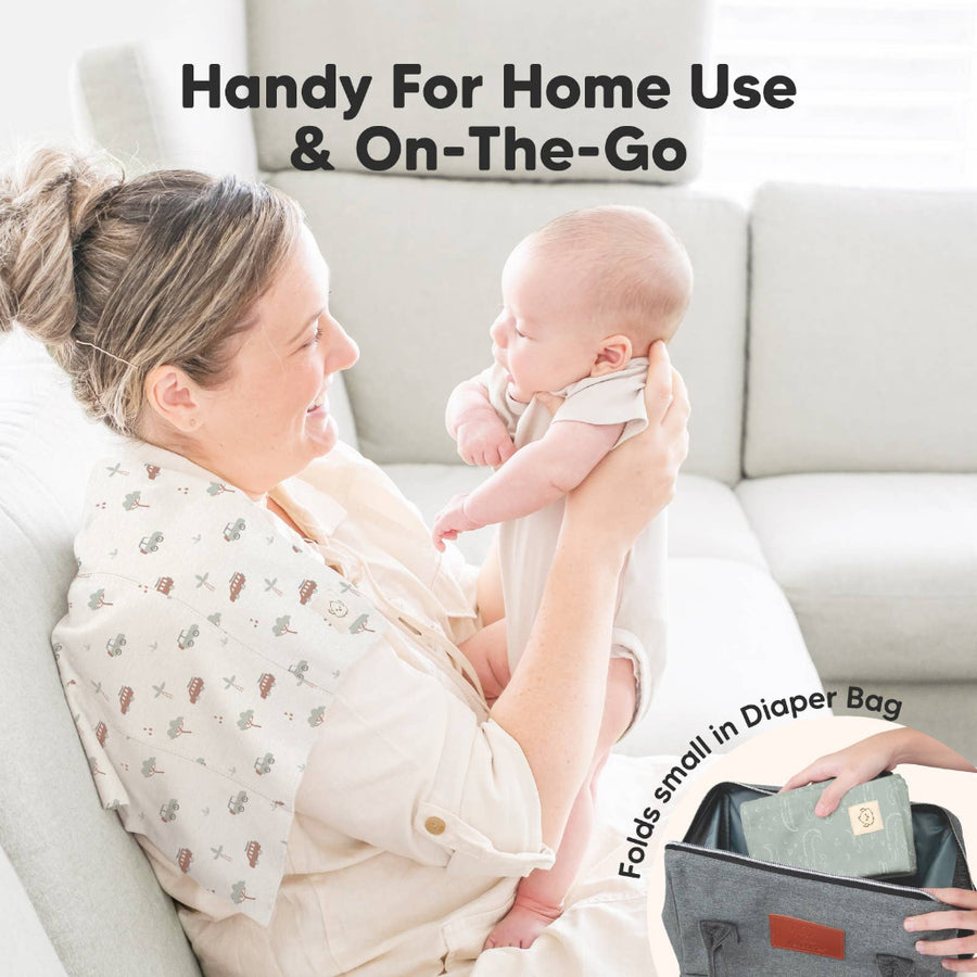 Woman holding a baby with a diaper bag labeled 'Handy For Home Use & On-The-Go' on a couch.