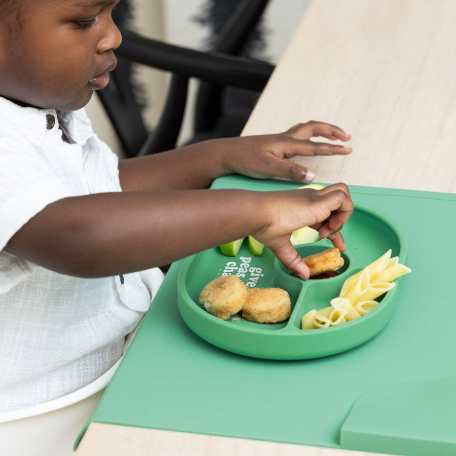 Child interacting with a green plate of food on a matching tray.