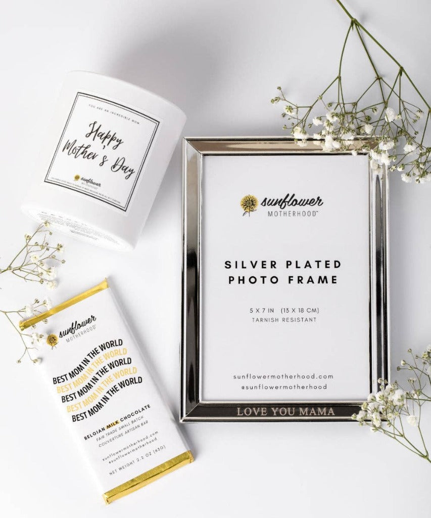 Image of the photo frame on a white table surrounded by a Happy Mother's Day candle, a Best Mom in the World chocolate bar, and sprigs of white baby's breath