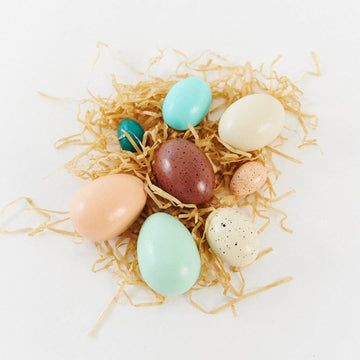 set of wooden painted eggs of various sizes and colors in a nest of paper straw
