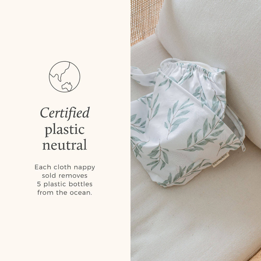 White cloth nappy with green leaf pattern on a beige couch, featuring text about plastic neutrality.