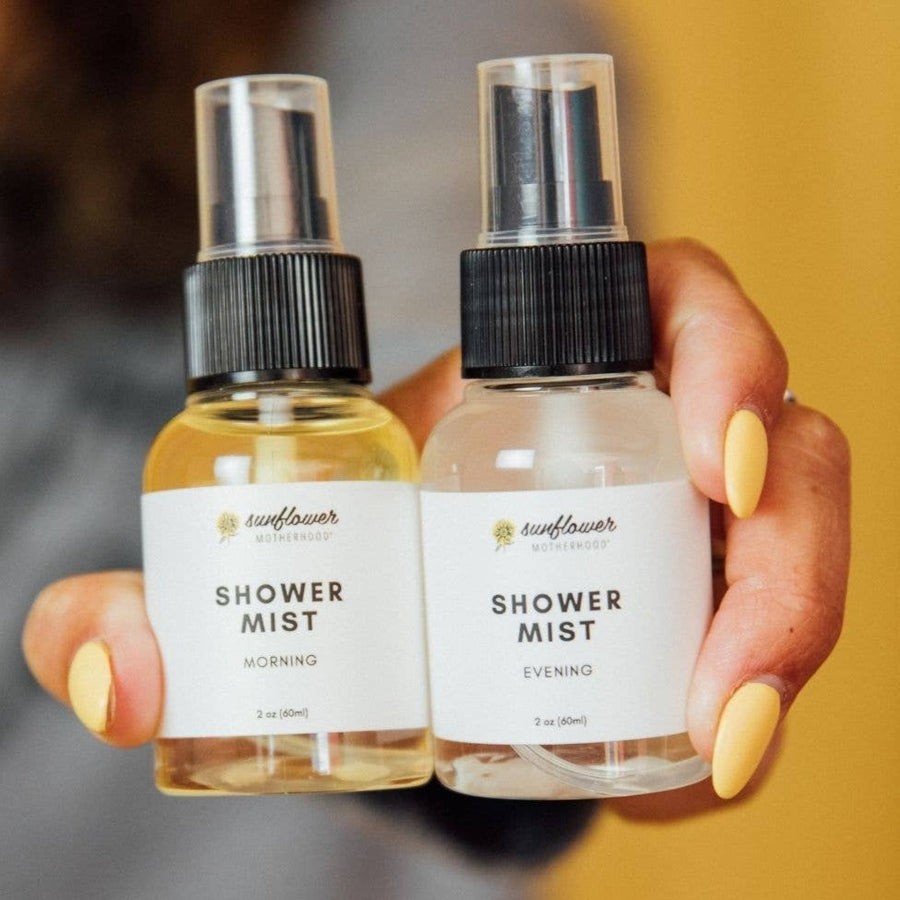 Image shows the Morning & Evening Shower Mist bottles in a person's hand with a medium light skin tone and long pale yellow painted nails