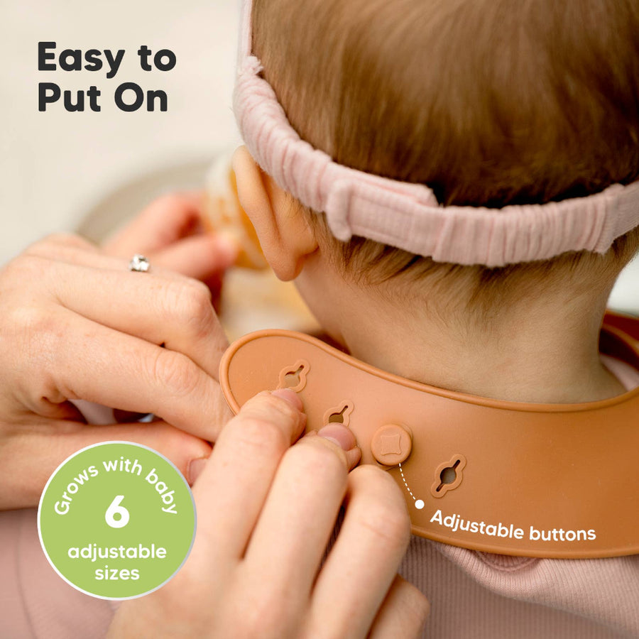 Baby wearing a bib with adjustable buttons, being put on by an adult hand.