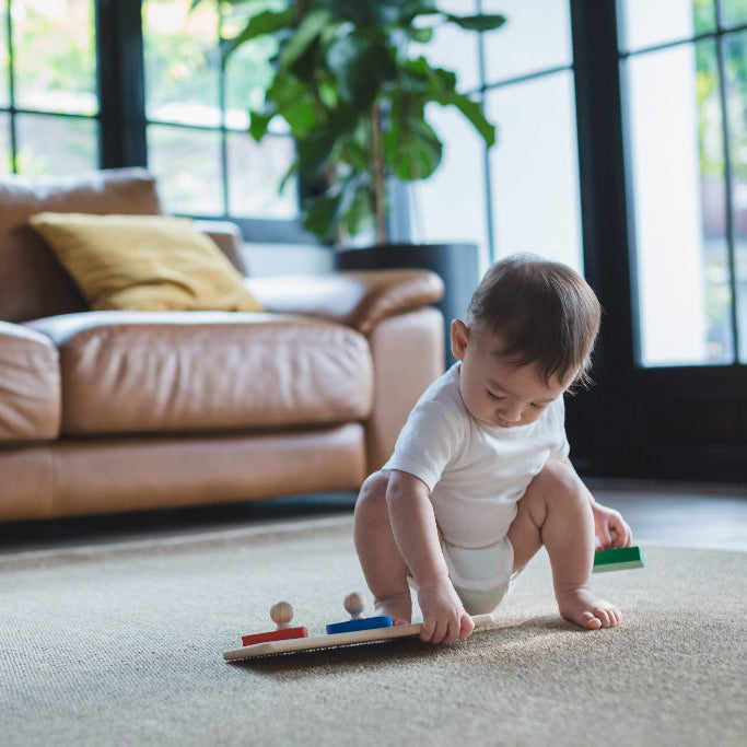 Baby playing with a toy on a carpeted floor in a living room.