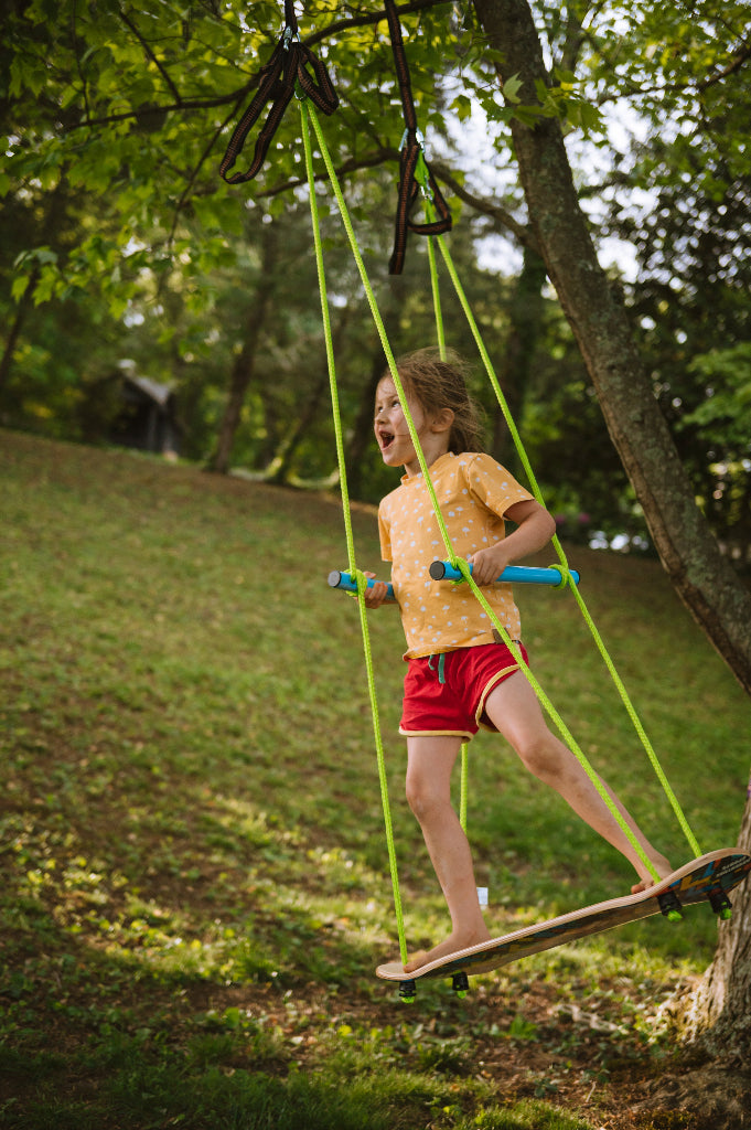 Child on a swing set in a park with trees and grass in the background