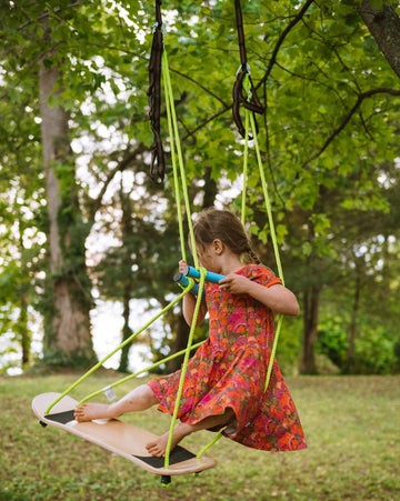Child in a colorful dress standing on a swing set in a park with trees in the background