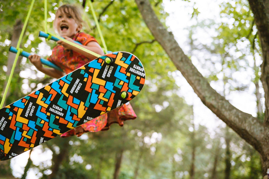Child on a swing with a colorful skateboard in the foreground, surrounded by trees.