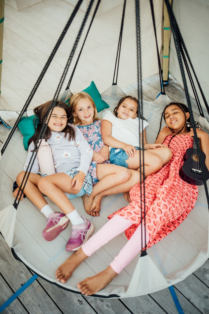Four children sitting on a round white swing with a wooden floor background