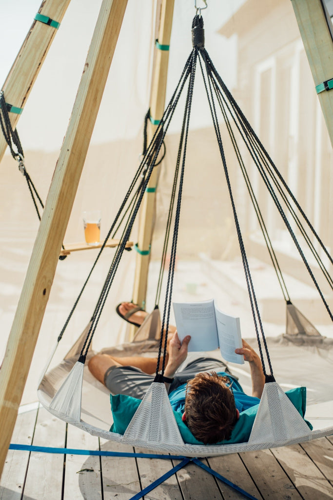 Person reading a book in a hanging chair on a wooden deck.