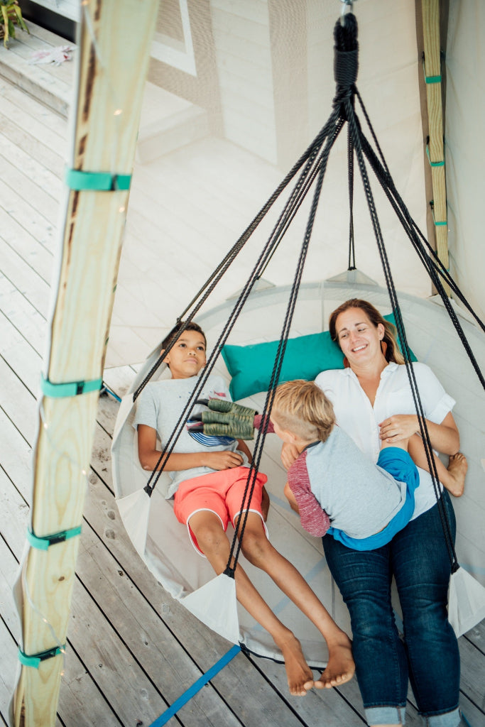 Woman and two children sitting in a hanging chair on a wooden deck.