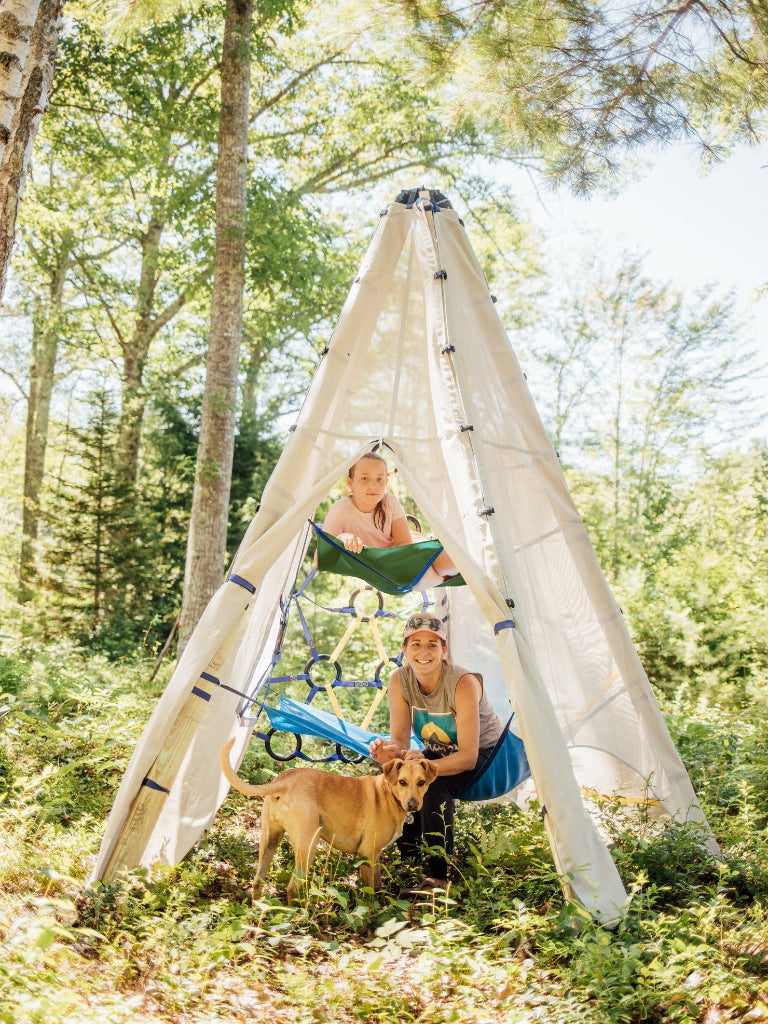 Two people with a dog inside a white teepee structure in a forest setting