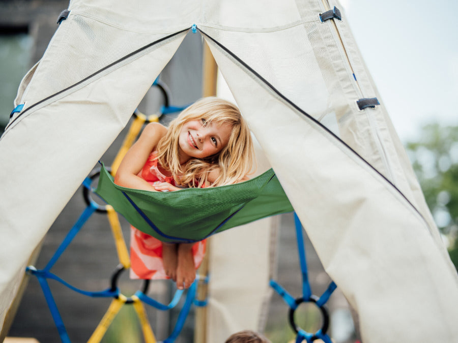 Child hanging from a green hammock inside a white teepee structure.