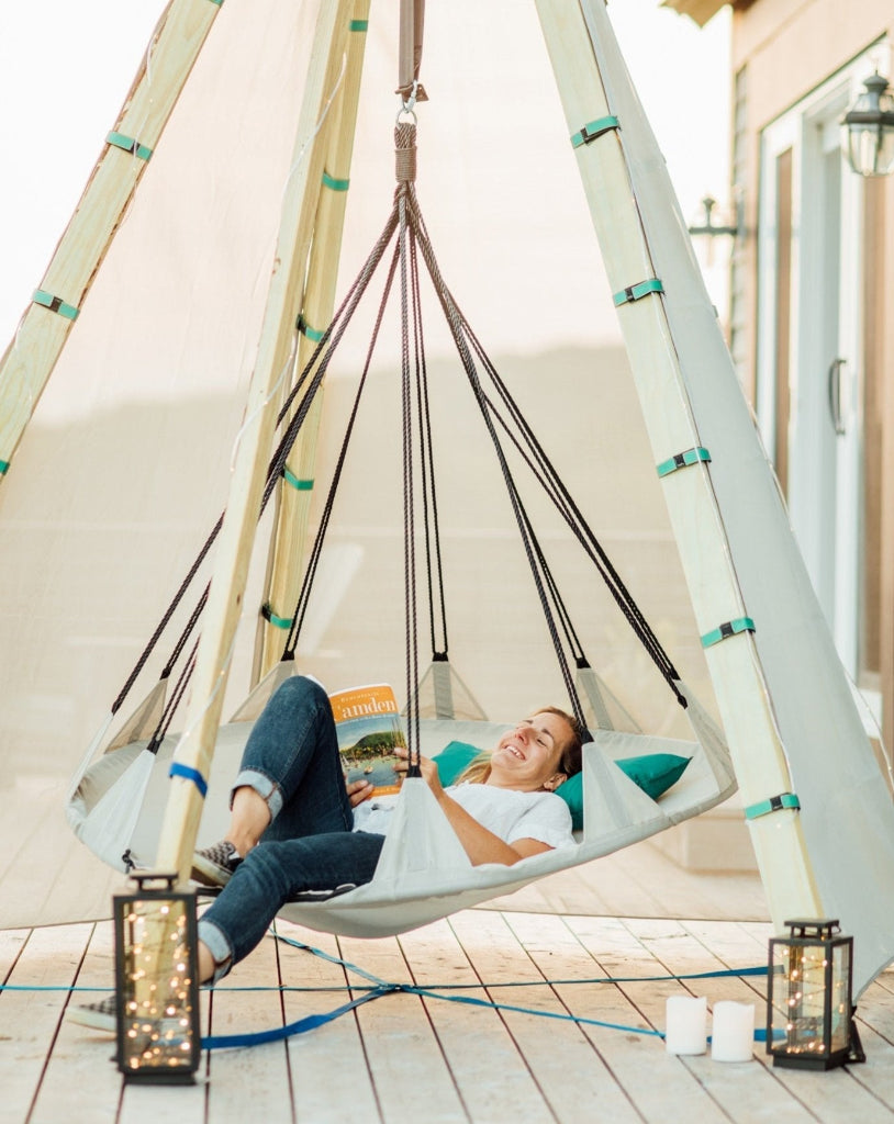 Person relaxing in a hanging chair on a wooden deck with a magazine