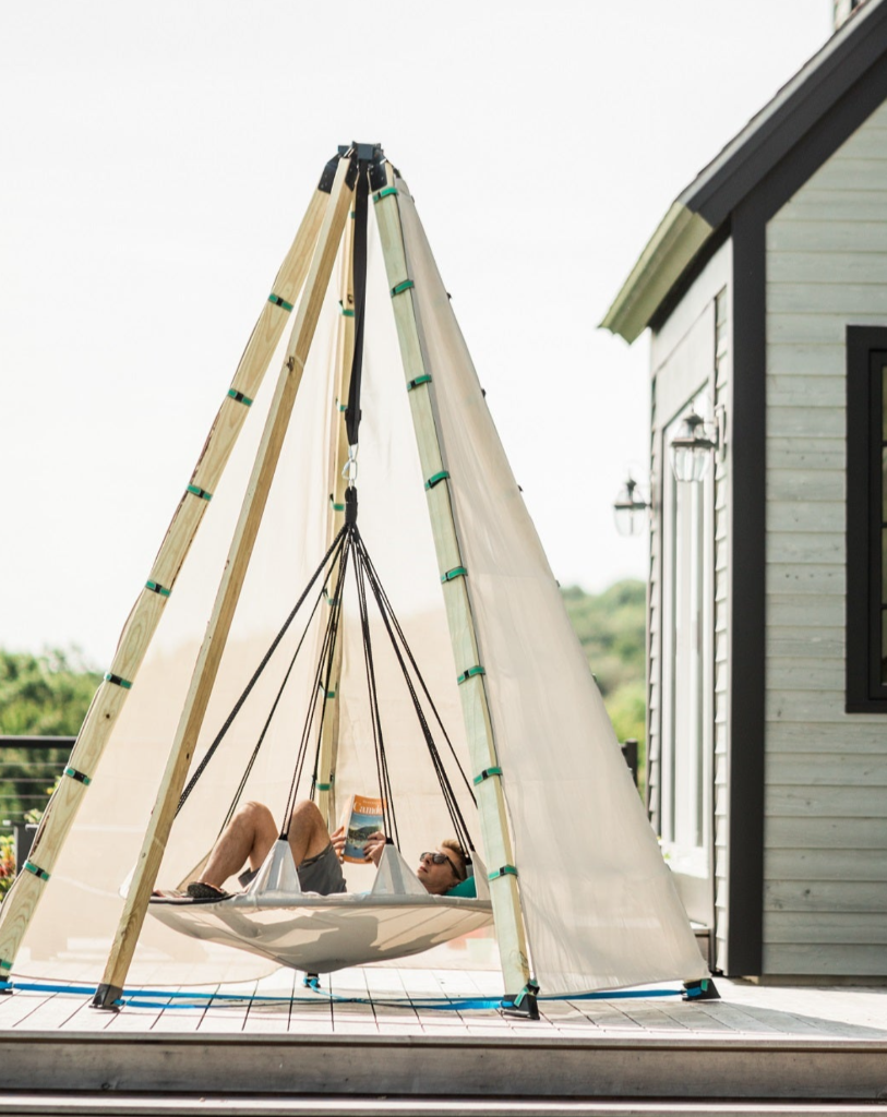 Person relaxing in a hanging chair on a deck with a house in the background