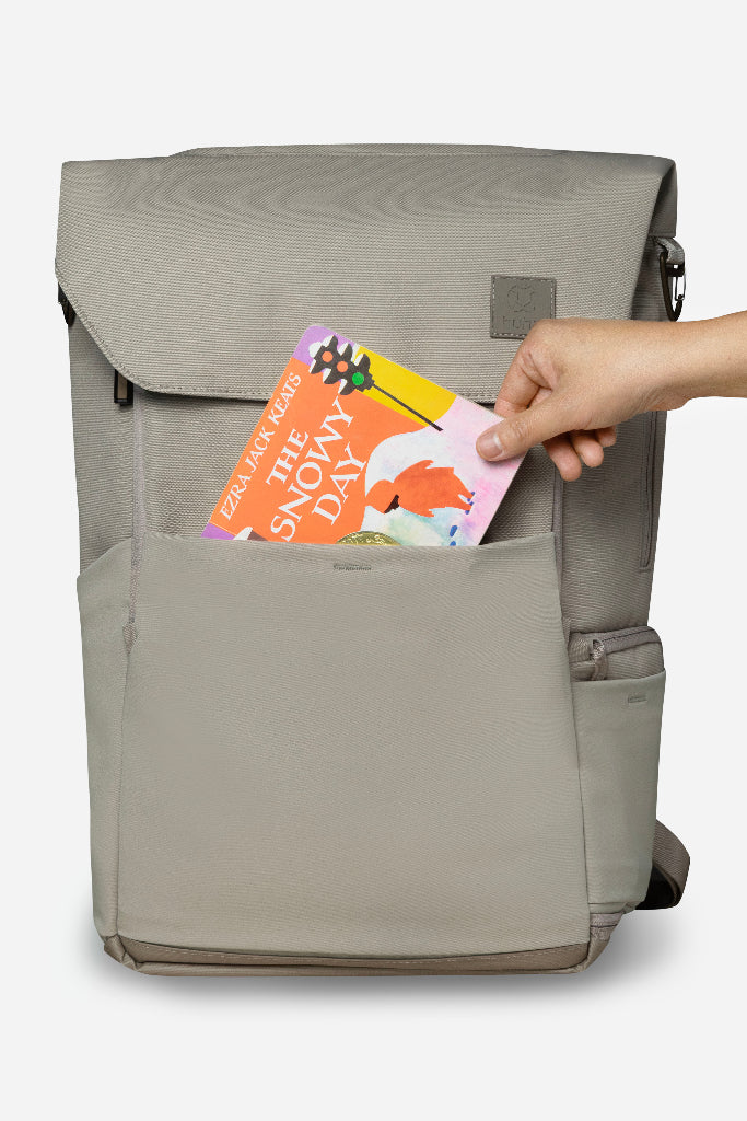 Gray backpack with a hand placing a book into its pocket on a white background