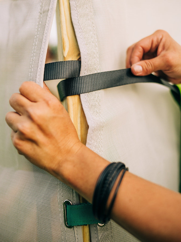 Person adjusting a strap on a tent with a neutral background