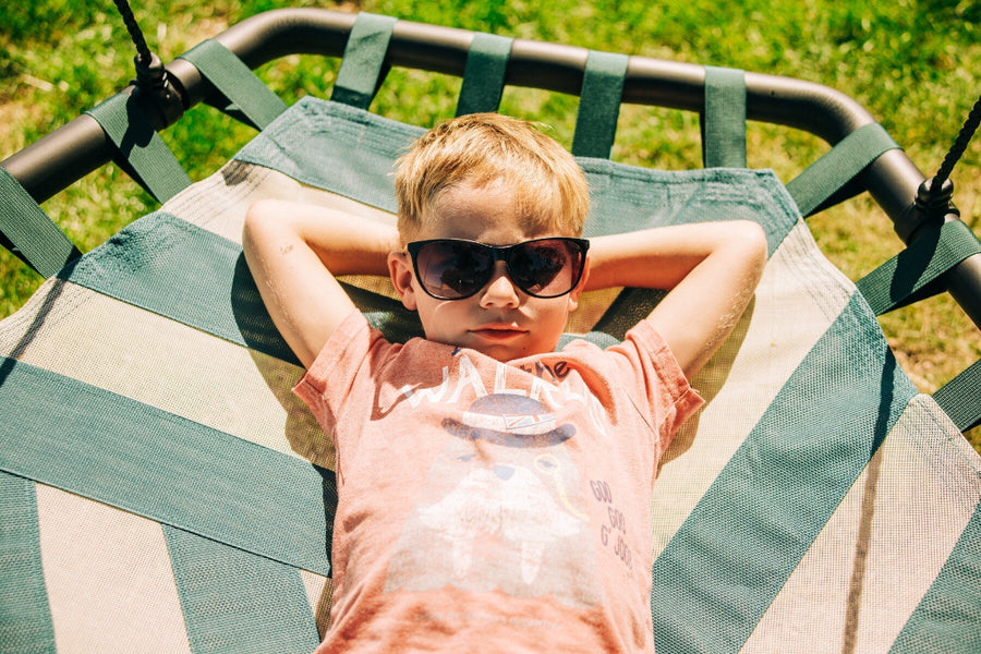 Child wearing sunglasses lying on a striped hammock outdoors