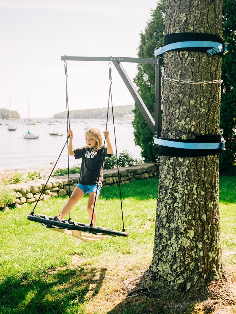 Person swinging on a tree swing with a scenic background of water and boats.