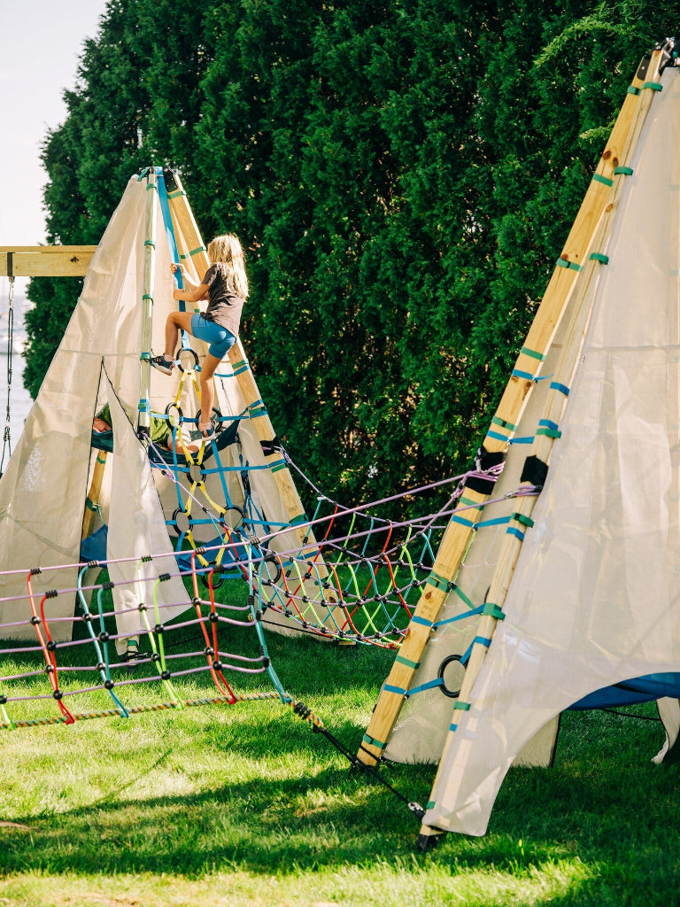Child playing on a rope ladder in a grassy area with trees in the background