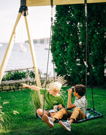 Two children on a swing set in a garden with a scenic background