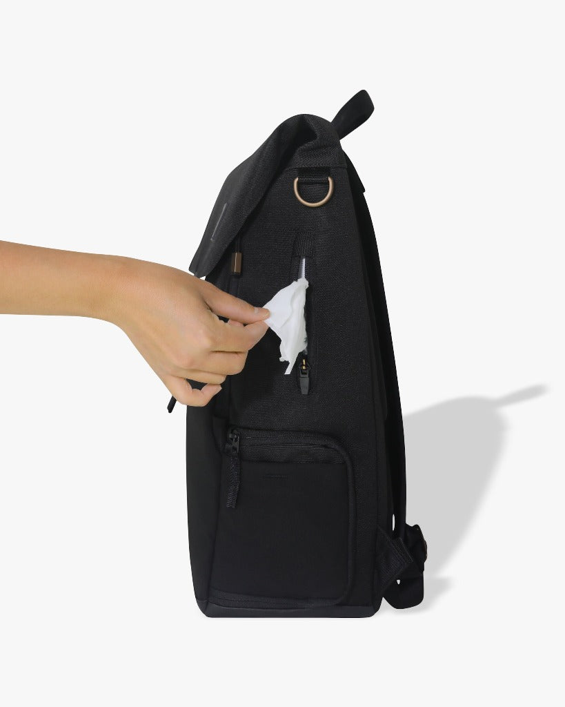 Picture of a side view of the backpack showing a light-skinned hand removing a wipe from the zippered wipes pocket