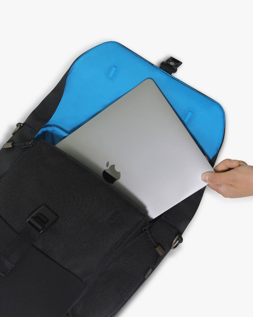 Picture of the backpack laying flat on a white surface with the top open and a light-skinned hand is removing a silver Apple laptop from the backpack