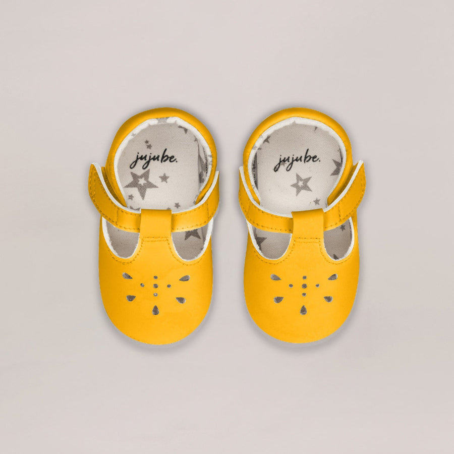 Pair of yellow baby shoes with 'juju.be' branding on a light gray background