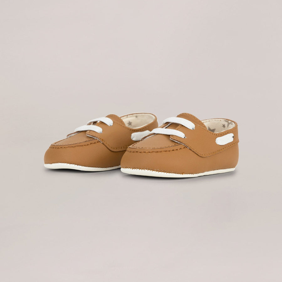 Pair of brown baby shoes with white soles on a beige background
