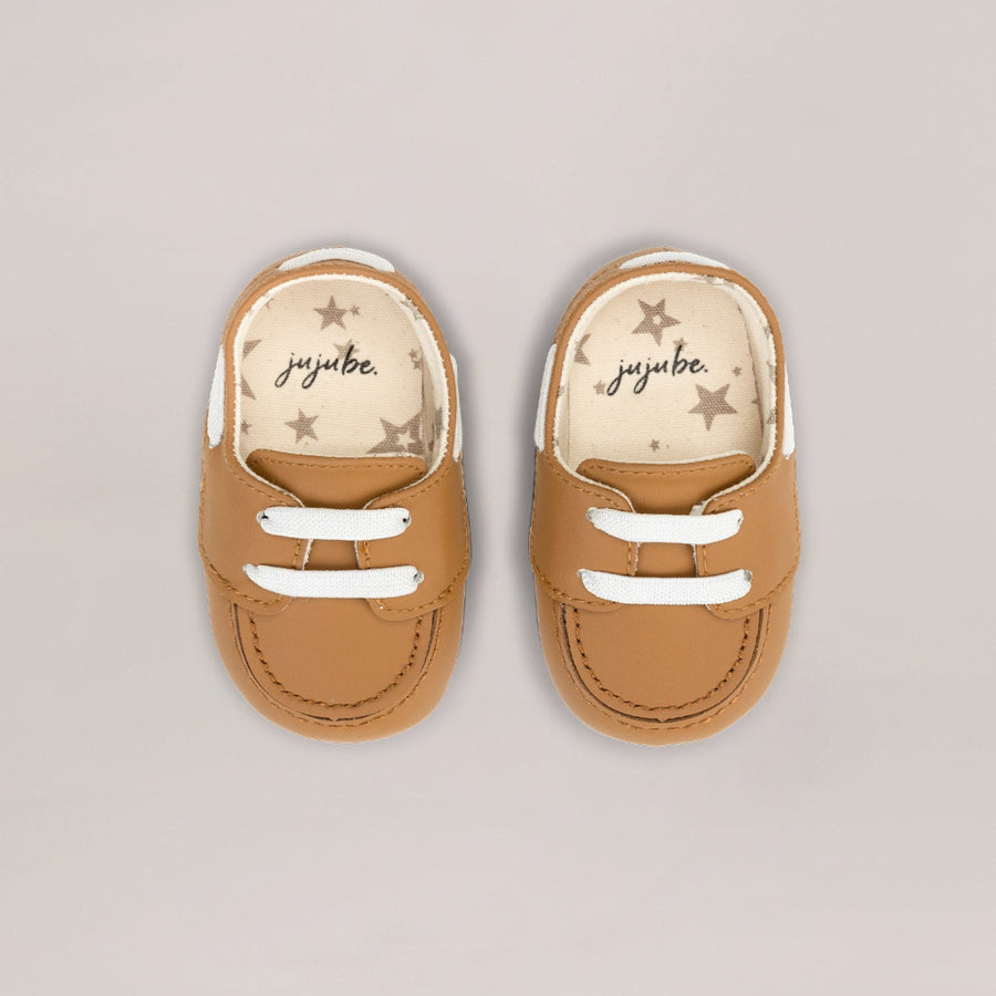 Pair of tan baby shoes with 'juuibe' branding on a light gray background