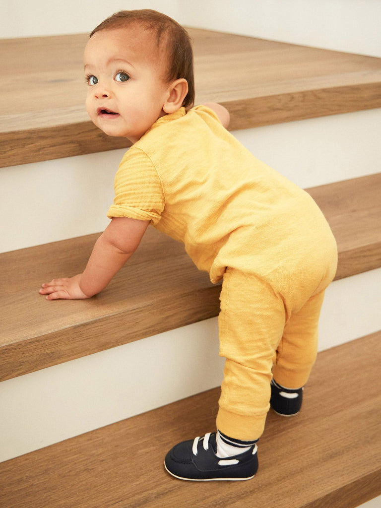 Baby in a yellow outfit standing on wooden stairs