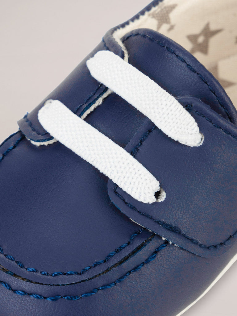 Close-up of a navy blue shoe with white laces on a neutral background